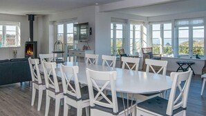 A spacious dining area with a round table and white chairs, a built-in fireplace, and large windows offering a view of the outdoors. - 5 Star Holiday Home in Ranum (Ranum)