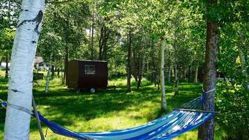 A hammock tied between trees in a grassy area with a trailer in the background.