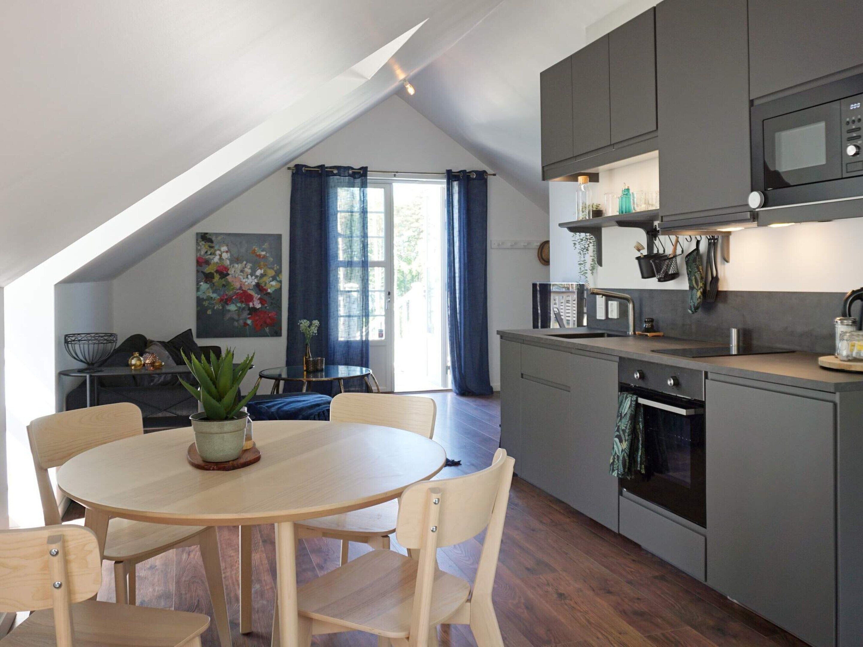 A modern kitchen with a dining area, featuring a round table, chairs, and a view of the outdoors through a window.