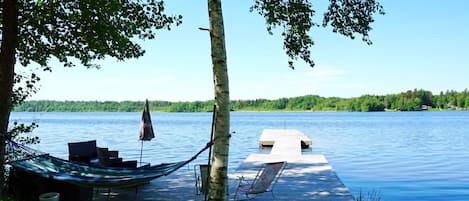 A wooden dock extending into a calm lake, surrounded by lush greenery and a clear sky.