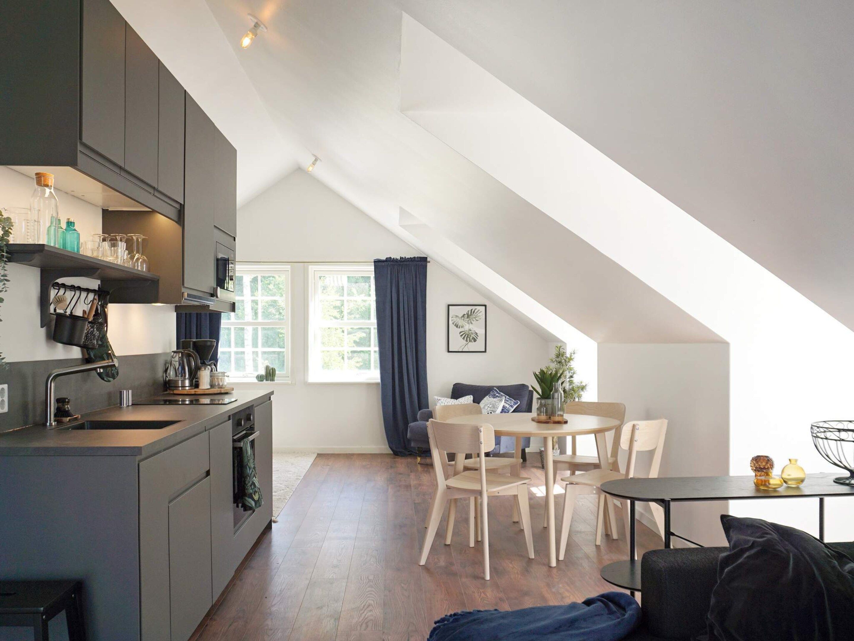 A modern kitchen with a dining area, wooden flooring, and a loft-style ceiling.
