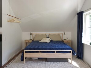 Une chambre à coucher avec un lit en bois, deux tables de chevet, un portant à vêtements et une fenêtre avec des rideaux.