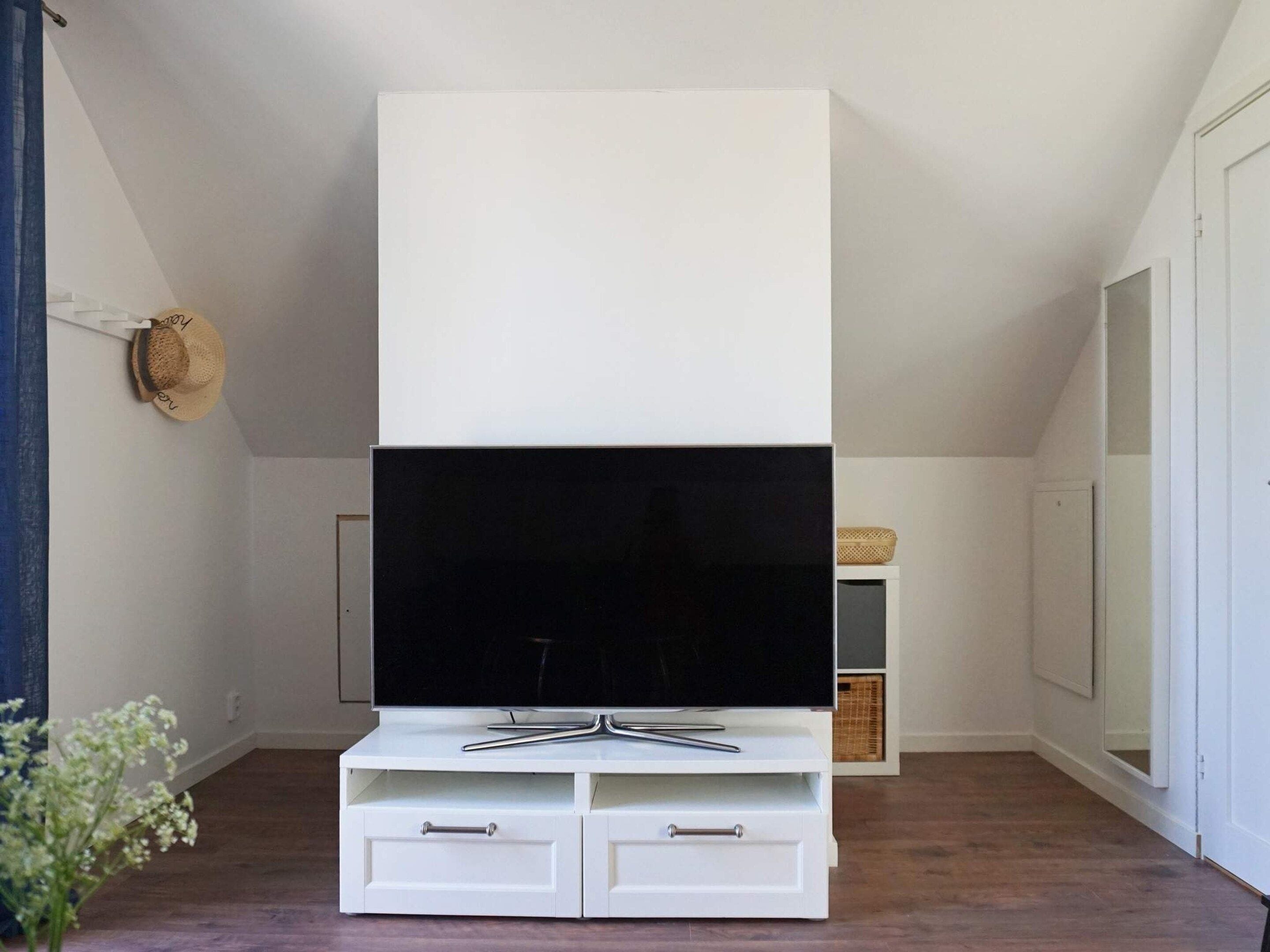 A modern living room with a flat-screen TV on a white entertainment unit, wooden flooring, and a small plant.