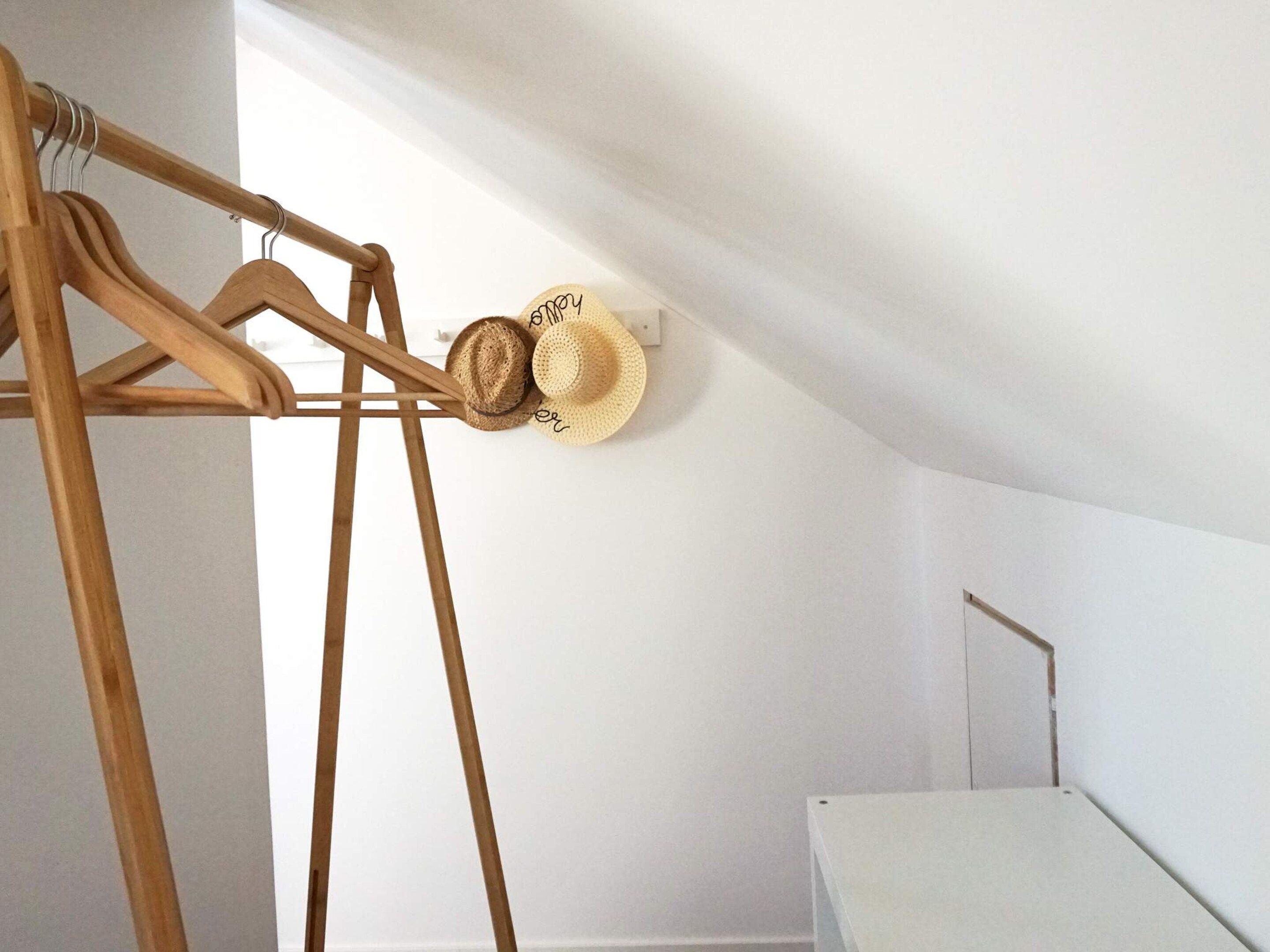 Een houten kledingrek met hoeden en een witte tafel in een kamer met witte muren.