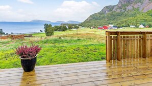 Une terrasse en bois agrémentée d’un pot de fleurs, offrant une vue sur un paysage côtier avec des maisons et des montagnes.