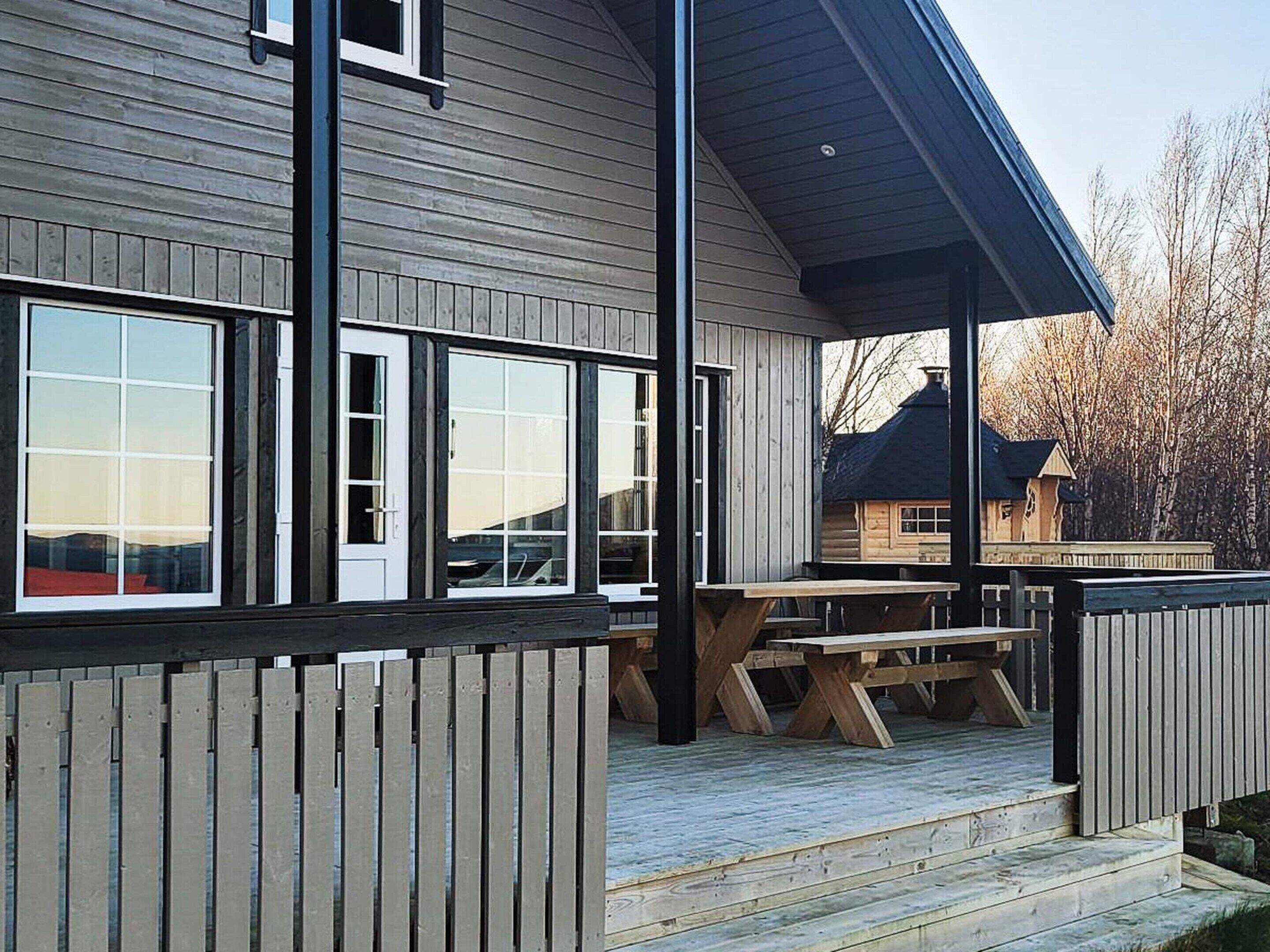 A wooden cabin with large windows, a covered patio, and a wooden deck.