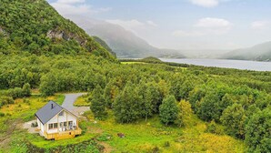 Une maison dotée d’un porche, entourée d’une végétation luxuriante et bordée d’un lac.