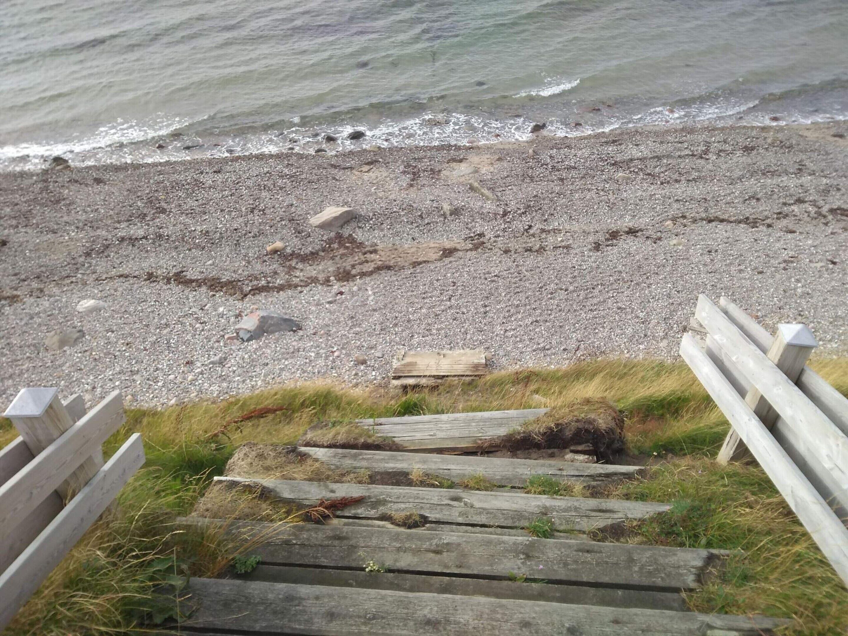 A wooden staircase leading down to a pebble beach with waves in the background.