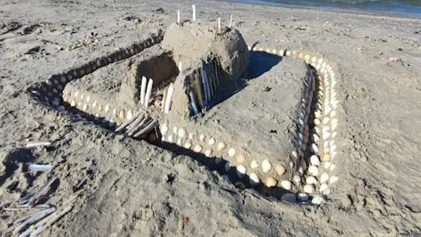 Un castell de sorra amb base quadrada i una torre central, envoltat d'un fossat de petits pedres.