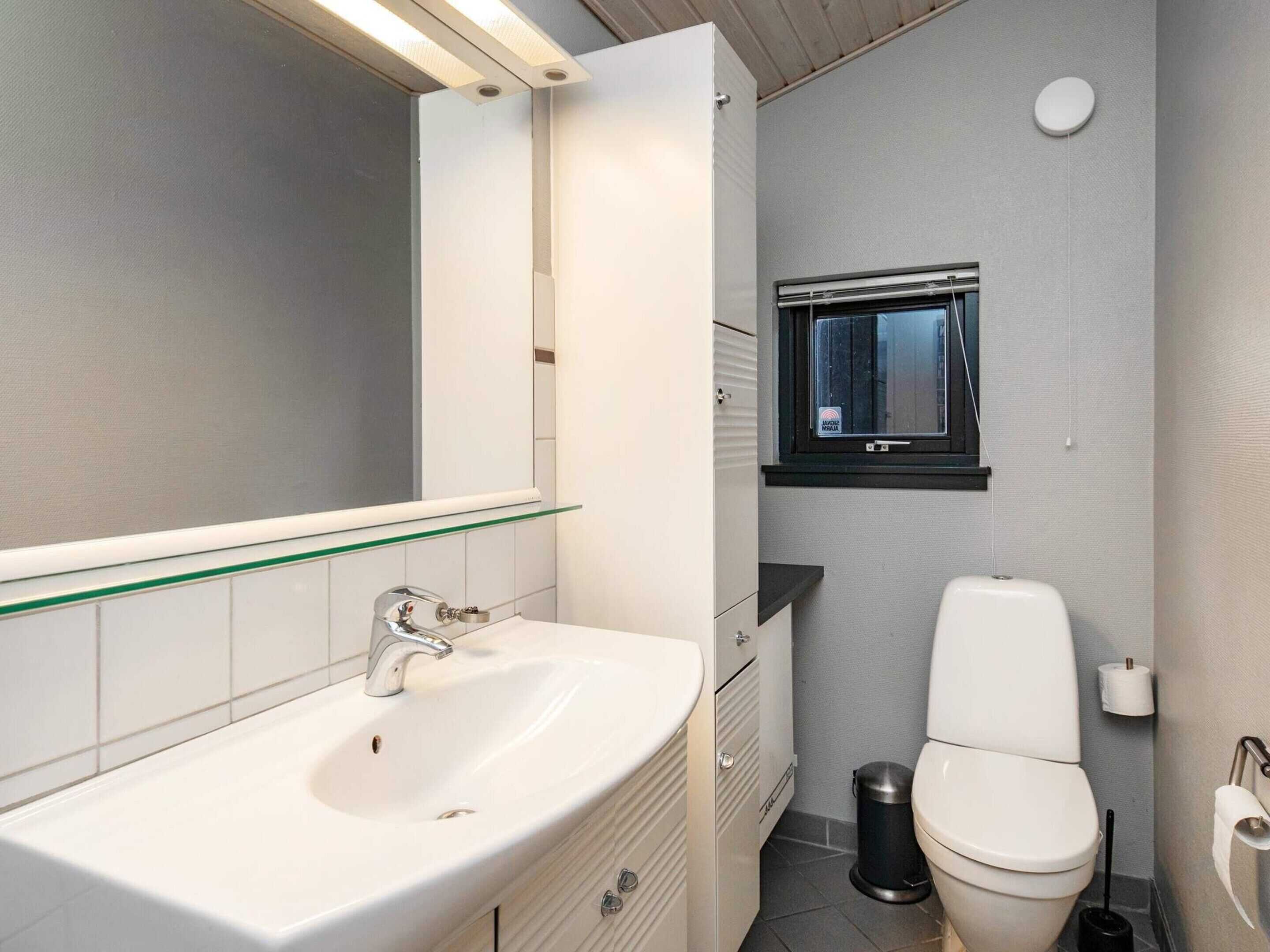 Un baño moderno con un lavamanos blanco, un espejo, un inodoro y una ventana pequeña.