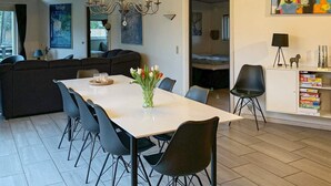 A modern kitchen with a dining area, featuring a chandelier, a white dining table with chairs, a vase of tulips, and a bookshelf with games. - 10 Person Holiday Home in Vaeggerlose-by Traum (Vaeggerlose)