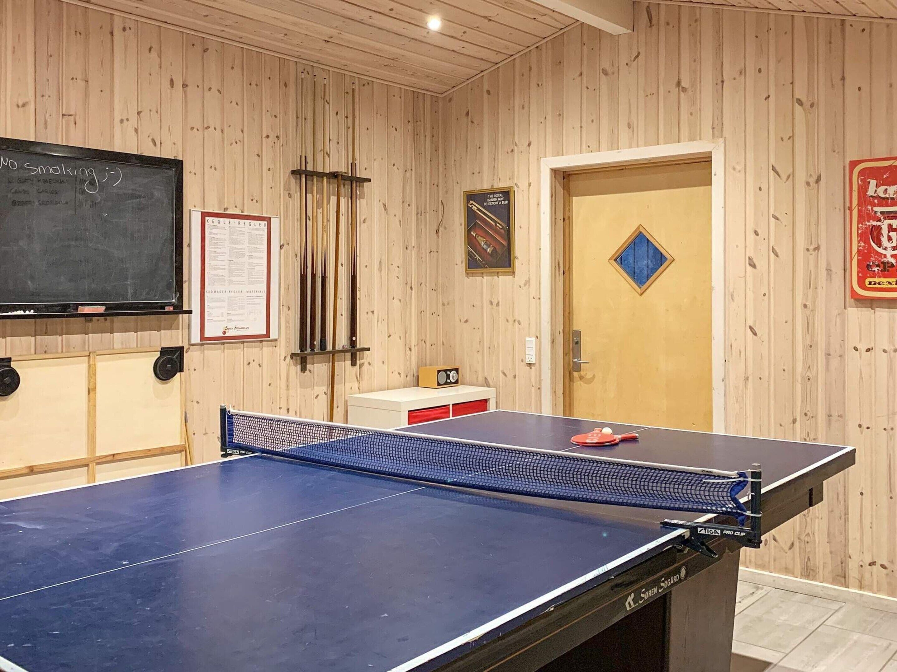 A ping pong table in a room with wooden walls, a chalkboard, and a door with a diamond-shaped decoration.