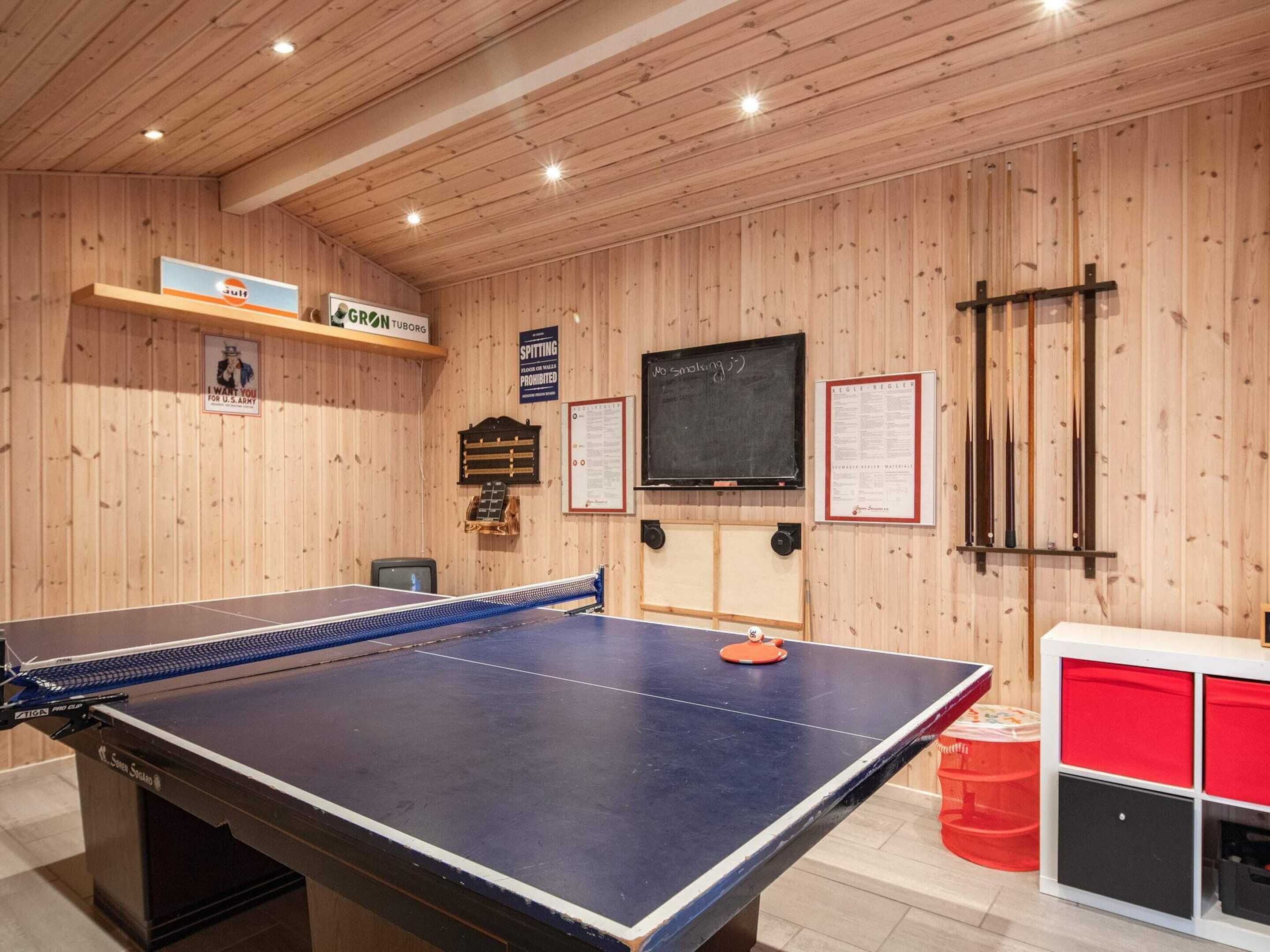 A ping pong table in a room with wooden walls, a chalkboard, and a red storage unit.