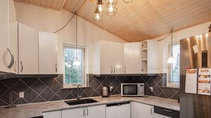 A modern kitchen with white cabinets, a built-in microwave, stainless steel appliances, and a window with blinds. - 10 Person Holiday Home in Vaeggerlose-by Traum (Vaeggerlose)