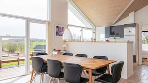 A modern dining area with a wooden table and black chairs, a kitchen with grey cabinets, and a view of the outdoors. - 4 Star Holiday Home in Nordborg (Nordborg)
