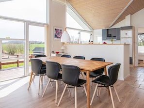 A modern dining area with a wooden table and black chairs, a kitchen with grey cabinets, and a view of the outdoors. - 4 Star Holiday Home in Nordborg (Nordborg)