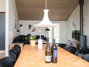 Et moderne spiseområde med et træbord, to vinflasker, en hvid pendellampe og en sort lædersofa i baggrunden.