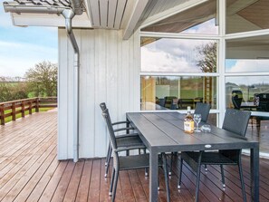 An outdoor deck with a table and chairs, a bottle of wine, and a view of the landscape. - 4 Star Holiday Home in Nordborg (Nordborg)
