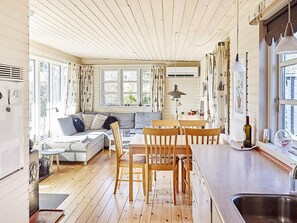 A cozy kitchen with wooden flooring, a dining area with wooden chairs, a built-in bench, and a large window with curtains. - 4 Person Holiday Home in Store Fuglede (Store Fuglede)