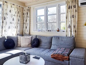 A cozy living room with a grey sofa, a small table, and a window with curtains. - 4 Person Holiday Home in Store Fuglede (Store Fuglede)