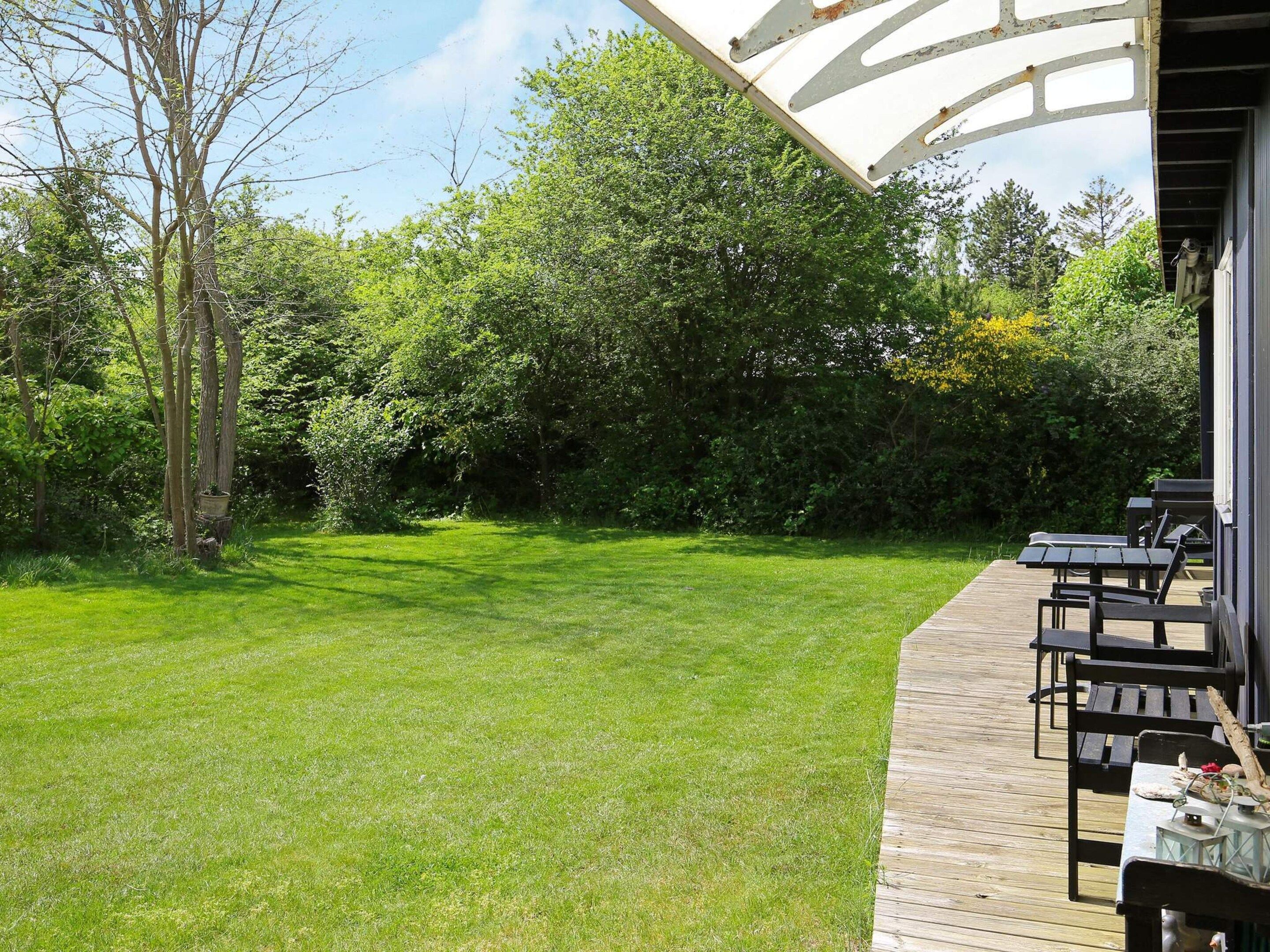A wooden deck with outdoor furniture, a grassy lawn, and dense foliage in the background.