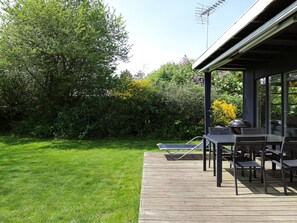 A wooden deck with outdoor furniture, a grill, and a view of a lush garden and trees. - 4 Person Holiday Home in Store Fuglede (Store Fuglede)