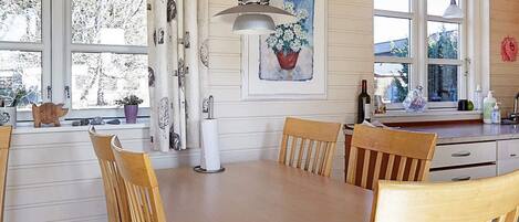 Une cuisine avec une table en bois, des chaises, une lampe suspendue, une fenêtre donnant sur un beau paysage et une plante en pot posée sur le rebord de la fenêtre.