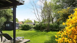 A well-maintained lawn with a wooden deck and outdoor furniture, surrounded by lush greenery and a small building. - 4 Person Holiday Home in Store Fuglede (Store Fuglede)