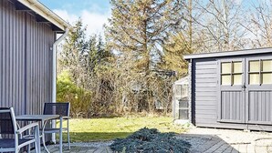 Un pati amb mobles d'exterior, una caseta i una zona de jardí amb arbustos i arbres.