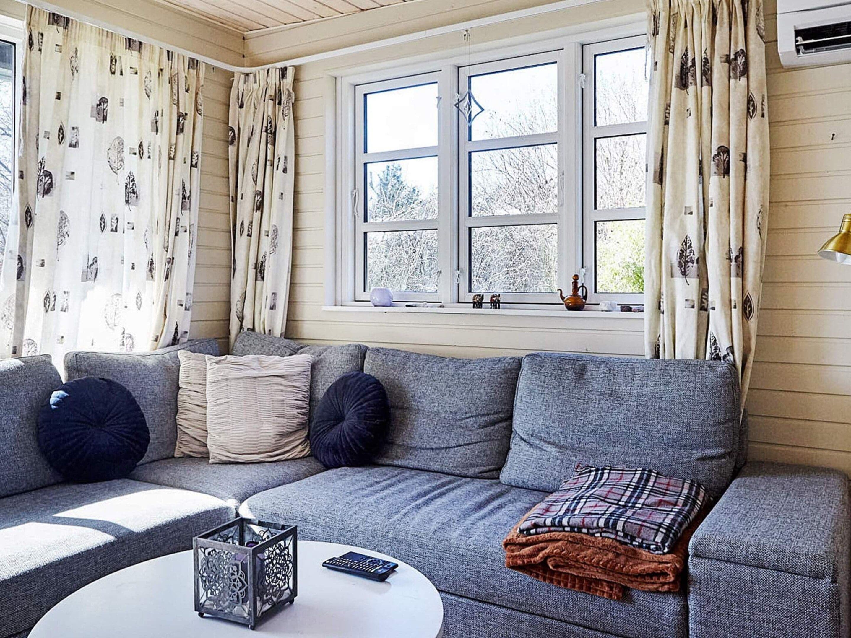 Ein gemütliches Wohnzimmer mit einem grauen Sofa, einem kleinen Couchtisch und einem Fenster mit Blick auf Bäume.