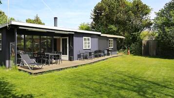 A modern house with a covered patio, a barbecue grill, and a lawn.