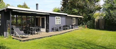Una casa moderna con un porche cubierto, una parrilla de barbacoa y un jardín.