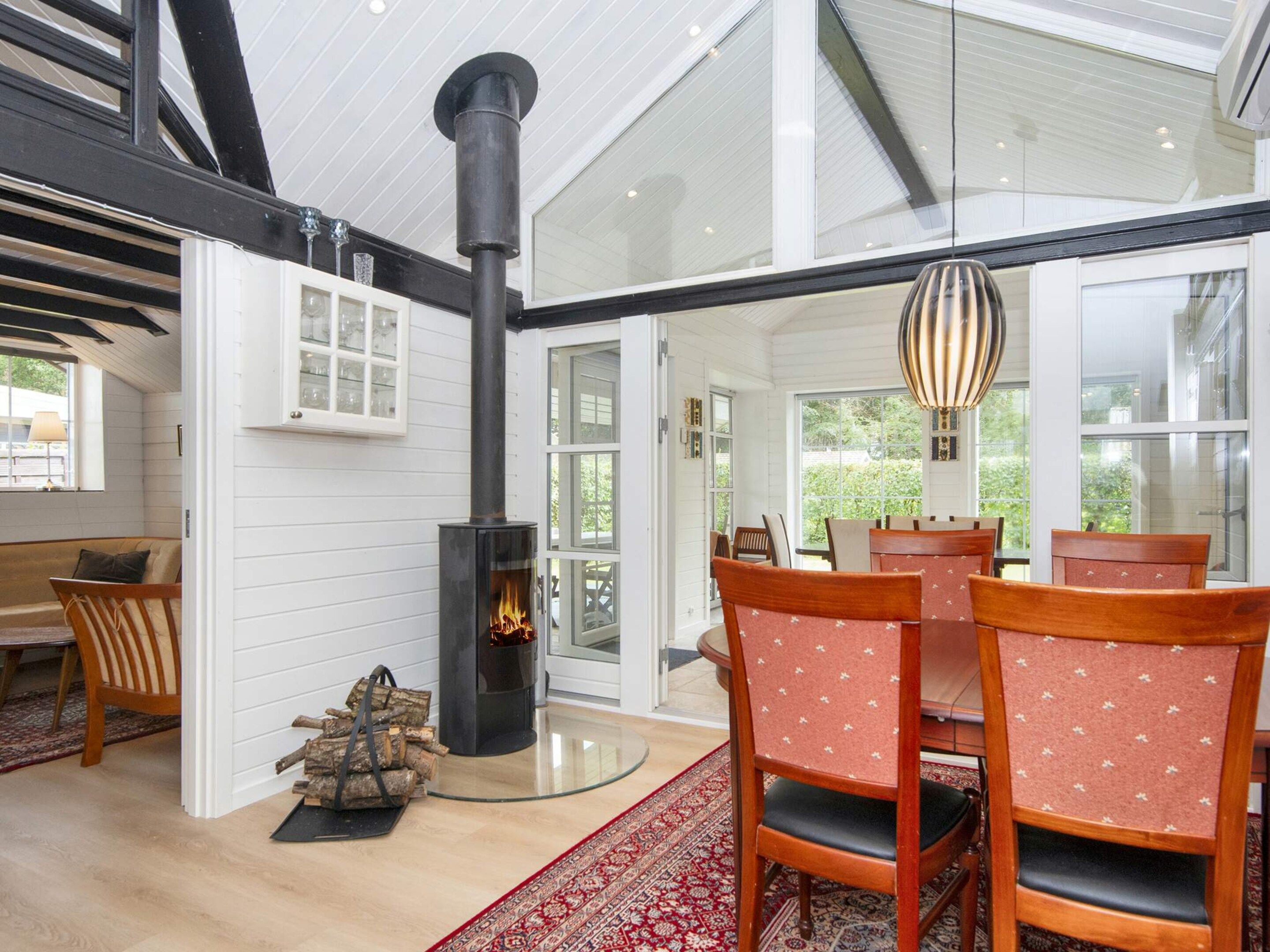 A modern interior with a wood-burning stove, dining area with chairs, and a glass door leading outside.