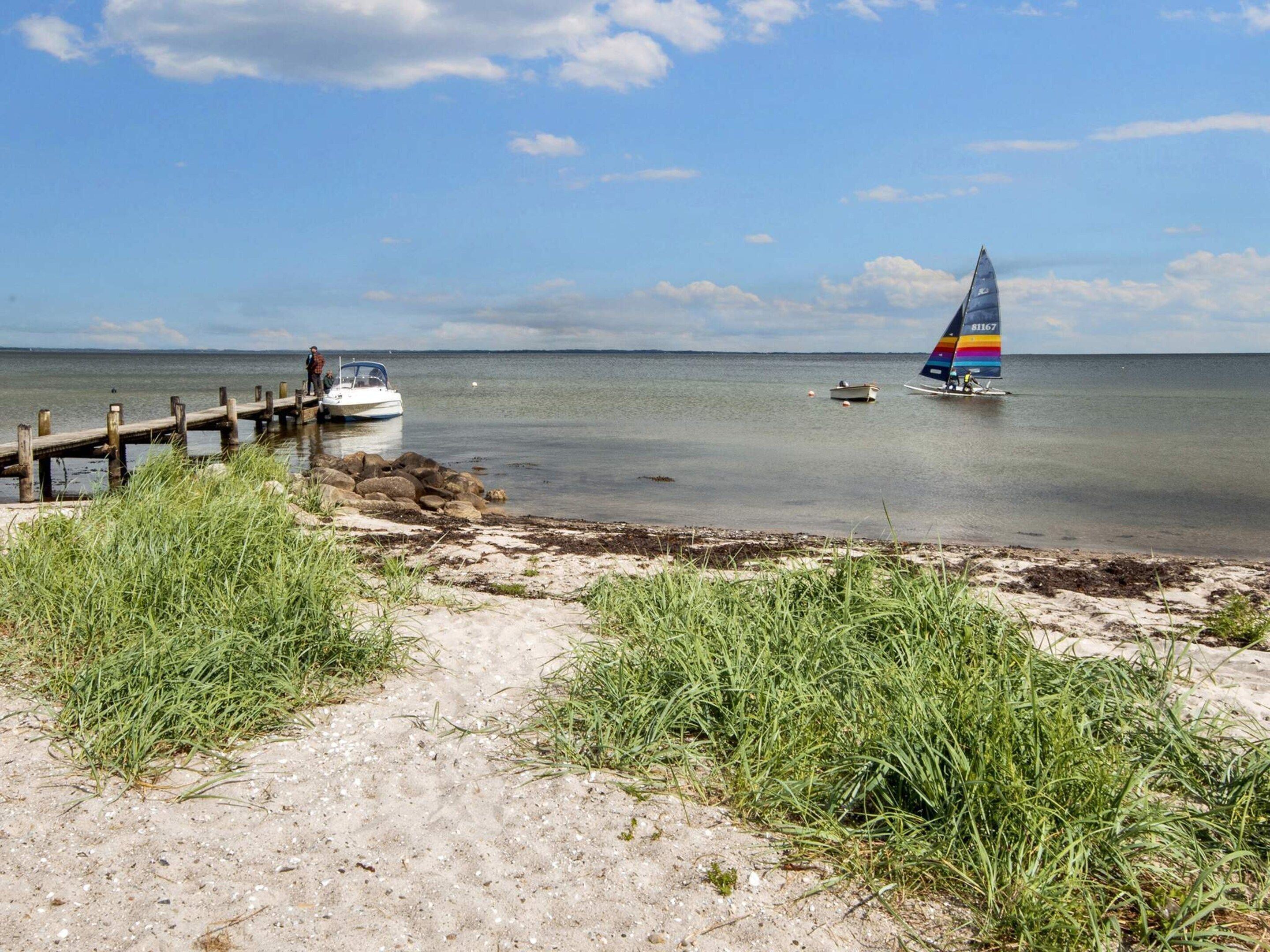 A sandy beach with a wooden dock, a sailboat, and a small motorboat.