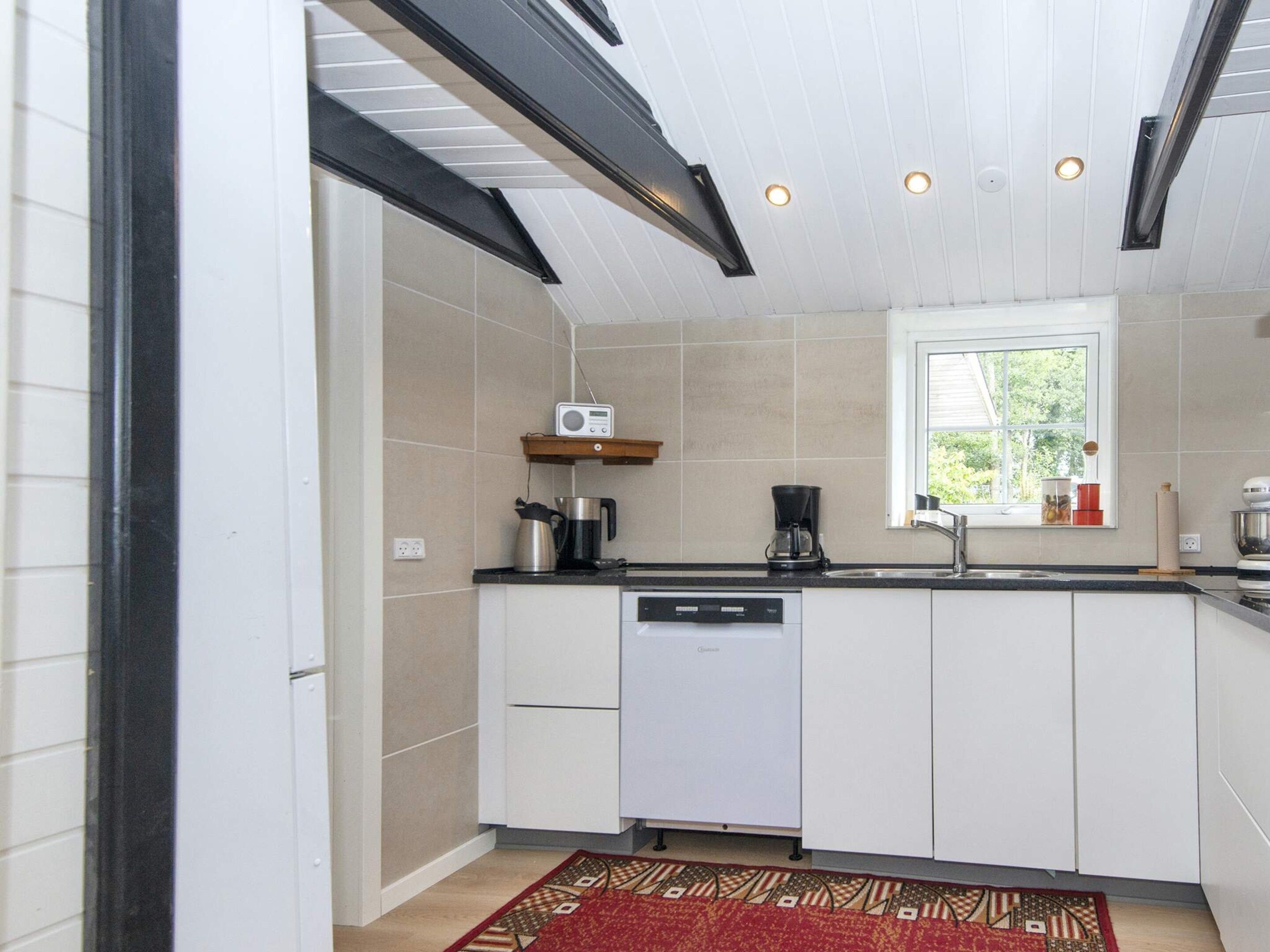 Cozinha moderna com armários brancos, máquina de lavar louça embutida, cafeteira e um rádio numa prateleira.