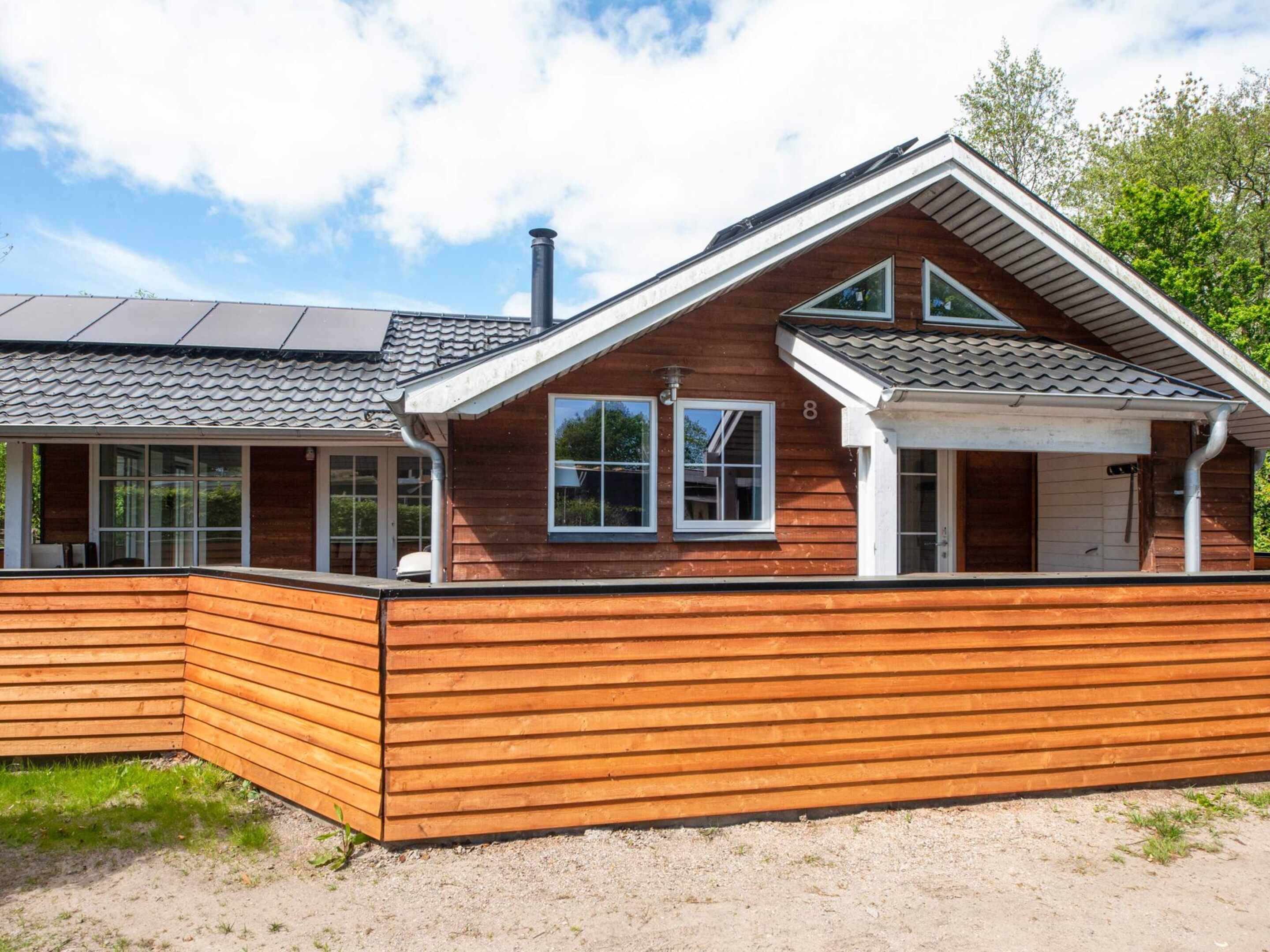 Een houten huis met twee verdiepingen, een schuin dak, grote ramen en een opvallende schoorsteen.