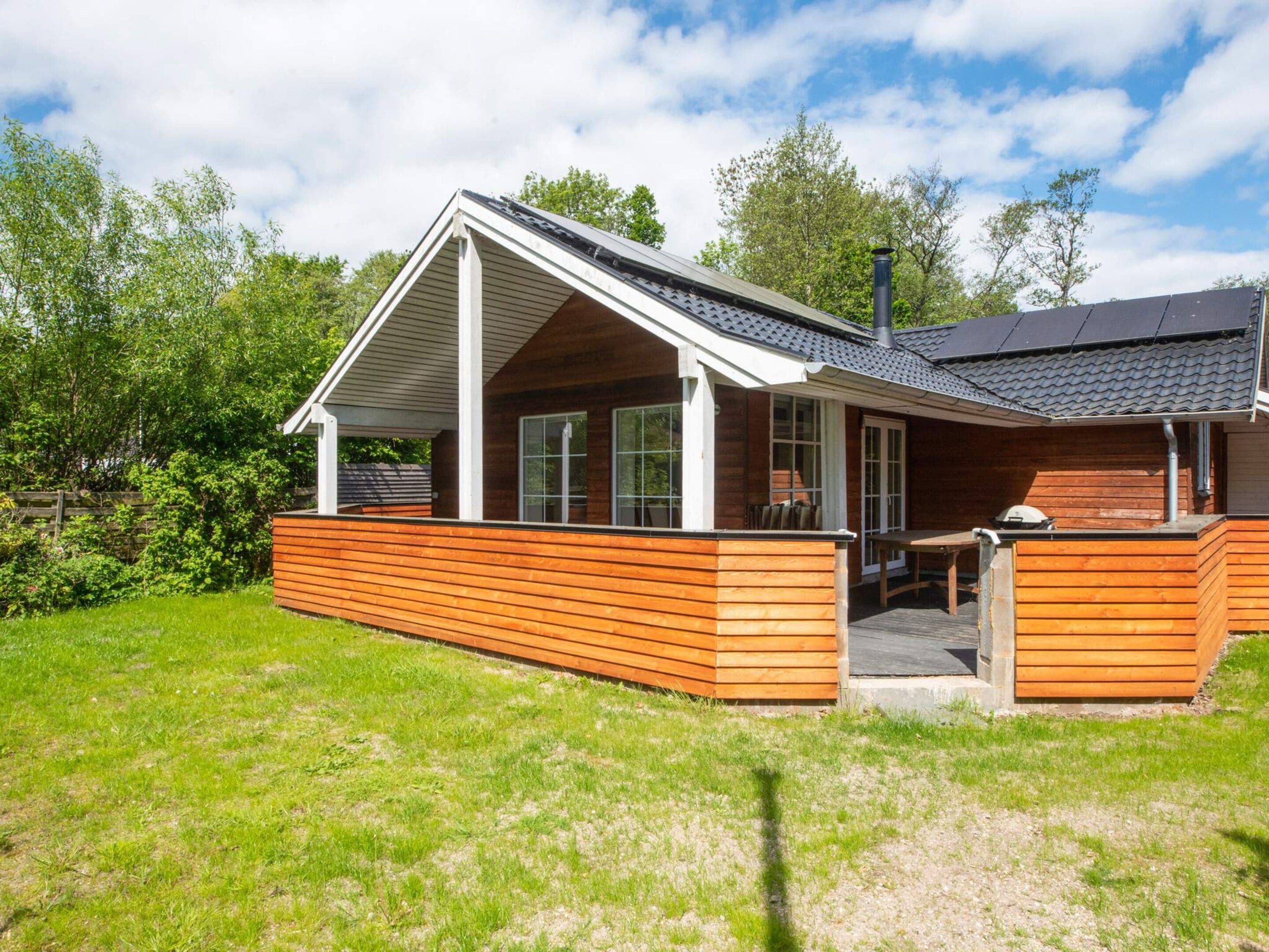 A modern wooden cabin with a covered patio, large windows, and a chimney.