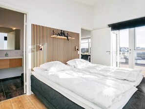 A modern bedroom with a large bed, a wooden slat headboard, a built-in bench, and a view of the outdoors.