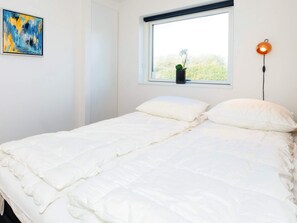 A bedroom with a bed, a window with a view, a wall-mounted lamp, and a painting.