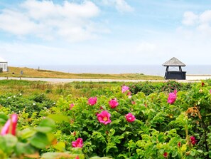 A coastal landscape with a gazebo, lush greenery, and a view of the sea.