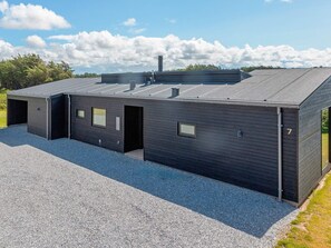 A modern building with a flat roof, multiple entry points, and a gravel driveway. - 5 Star Holiday Home in Lokken (Lokken)