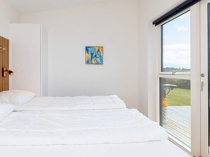A bedroom with a bed, a painting on the wall, and a window with a view of the outdoors. - 5 Star Holiday Home in Lokken (Lokken)