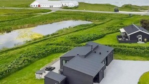 A modern building with a flat roof, surrounded by green fields and a body of water. - 5 Star Holiday Home in Lokken (Lokken)
