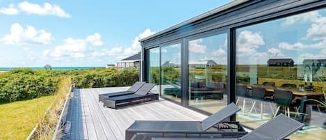 A modern outdoor deck with sun loungers and a glass wall overlooking a coastal landscape.