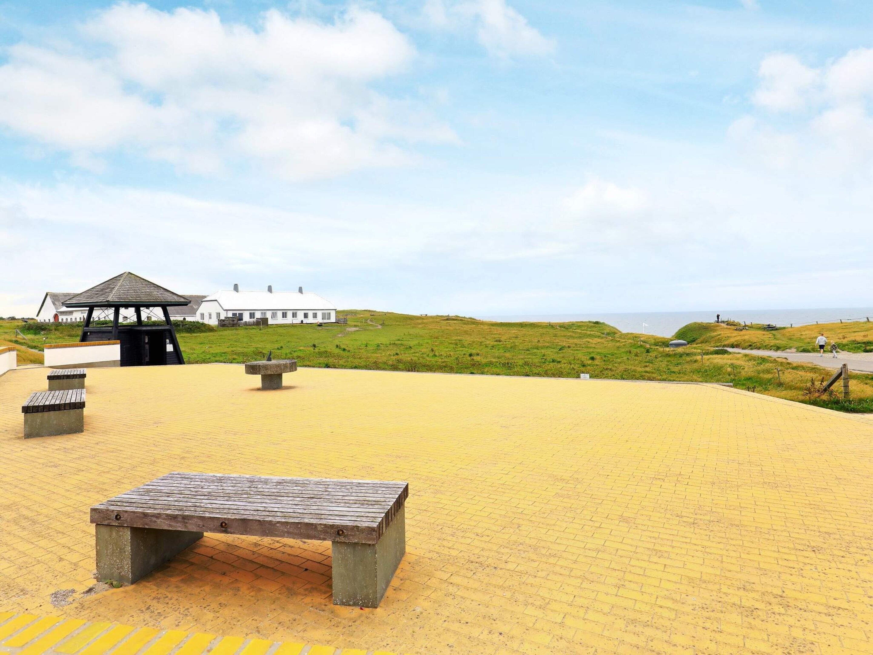 A sandy beach area with a wooden bench, a stone bench, and a gazebo.