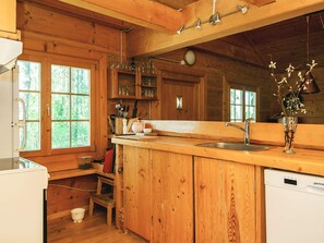 A wooden cabin kitchen with a wooden countertop, a sink, and a dishwasher. There are cabinets, a window, and a vase with flowers on the counter. - 8 Person Holiday Home in Ebeltoft (Ebeltoft)