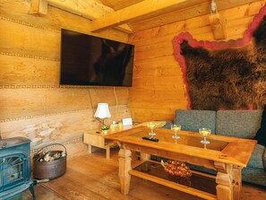 Una habitación acogedora de madera con un televisor grande en la pared, una mesa de madera con vasos y un revestimiento de piel rústico.