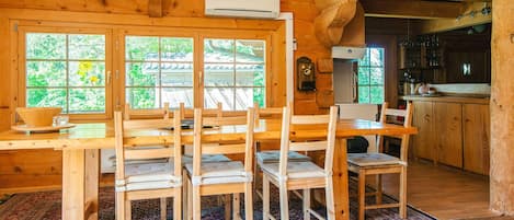 A wooden cabin interior with a dining area, kitchen, and large windows.