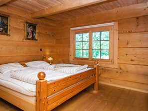 A wooden cabin room with a bed, a window, and two paintings on the wall.