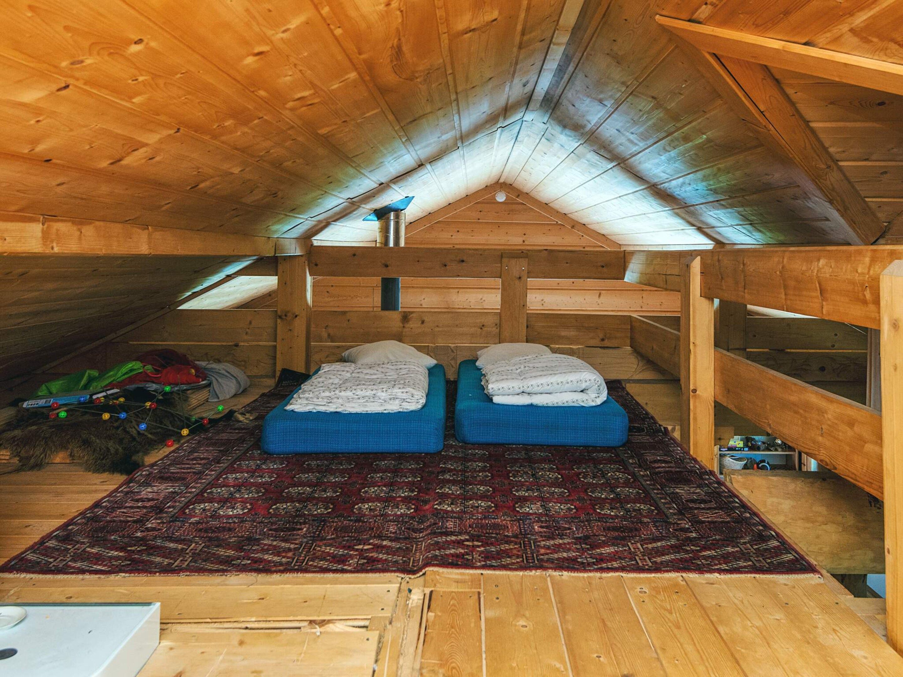 A wooden attic room with two bunk beds, a red patterned rug, and a skylight.